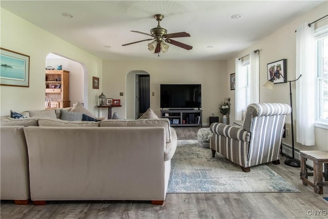 living area with ceiling fan, arched walkways, and wood finished floors