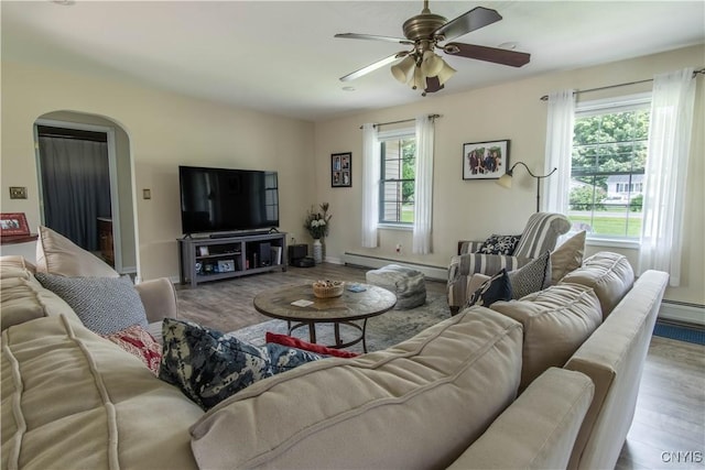 living room with arched walkways, baseboard heating, ceiling fan, and wood finished floors