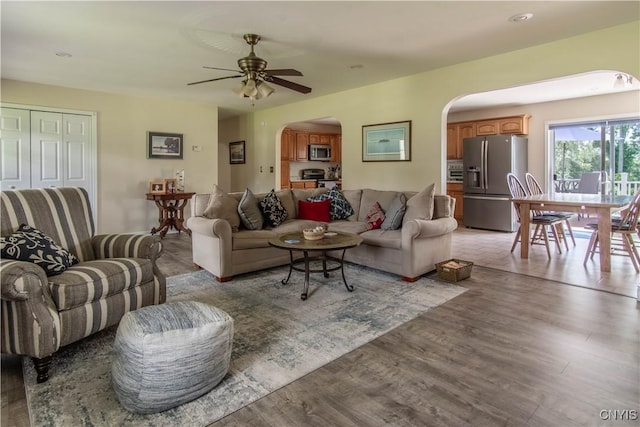 living room featuring arched walkways, light wood-style flooring, and a ceiling fan