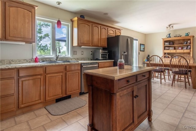 kitchen with a kitchen island, brown cabinetry, hanging light fixtures, stainless steel appliances, and a sink