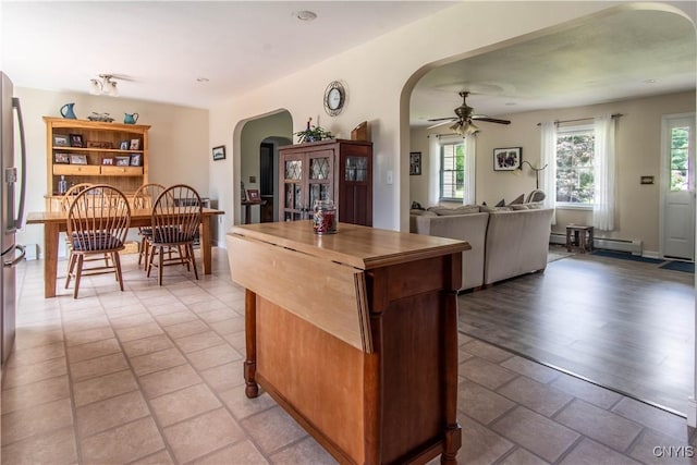 kitchen featuring arched walkways, ceiling fan, open floor plan, baseboard heating, and a center island