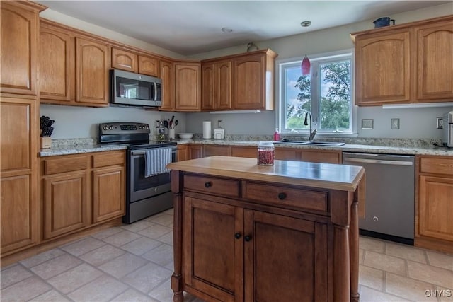 kitchen with a sink, pendant lighting, brown cabinetry, and stainless steel appliances