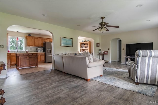 living room featuring arched walkways, baseboards, a ceiling fan, and wood finished floors