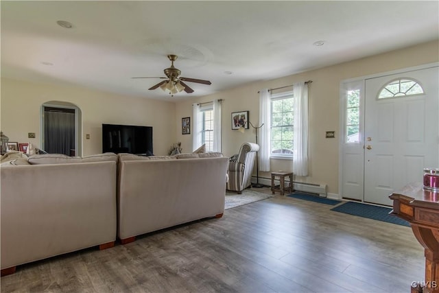 living room featuring arched walkways, baseboard heating, ceiling fan, and wood finished floors