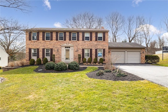 colonial-style house with concrete driveway, a front yard, an attached garage, brick siding, and a chimney