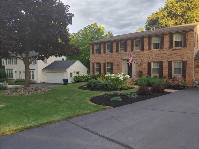 colonial house featuring brick siding, a garage, an outbuilding, and a front lawn