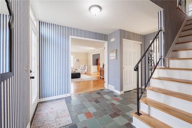 foyer entrance with stone tile flooring, stairway, wallpapered walls, and baseboards