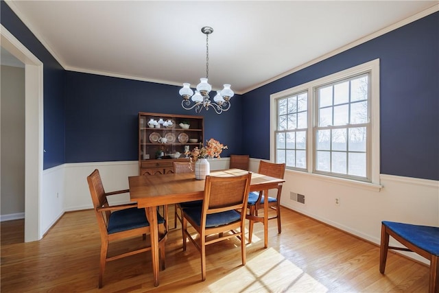 dining area with visible vents, wood finished floors, ornamental molding, and a chandelier