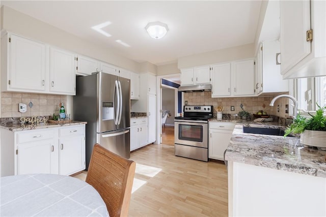 kitchen featuring under cabinet range hood, a sink, stainless steel appliances, light wood-style floors, and white cabinets