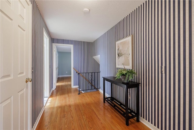 hallway featuring an upstairs landing, baseboards, wood finished floors, and wallpapered walls