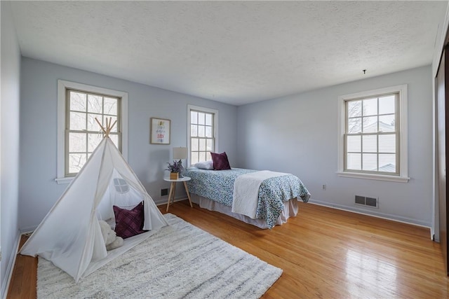 bedroom with visible vents, a textured ceiling, baseboards, and wood finished floors