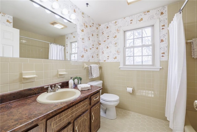 bathroom with wallpapered walls, tile walls, curtained shower, and a wainscoted wall