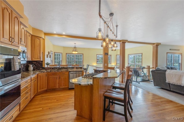 kitchen with dark stone countertops, a breakfast bar area, decorative columns, appliances with stainless steel finishes, and open floor plan