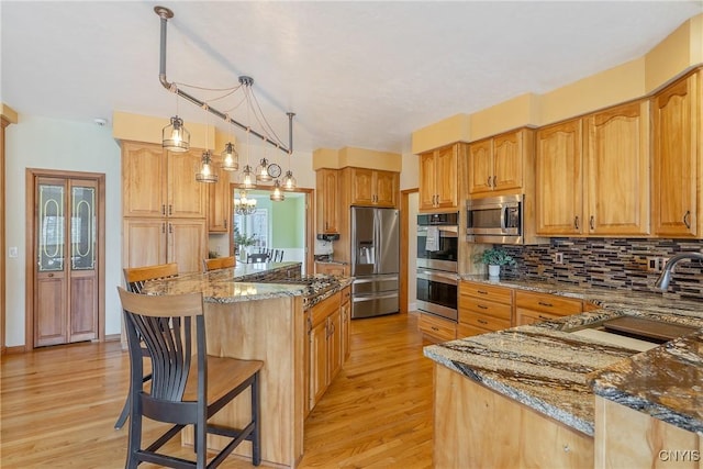 kitchen featuring a breakfast bar, stone countertops, decorative backsplash, light wood-style floors, and appliances with stainless steel finishes