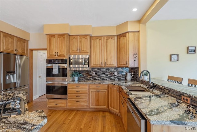 kitchen with light wood-style flooring, a sink, stone countertops, stainless steel appliances, and decorative backsplash