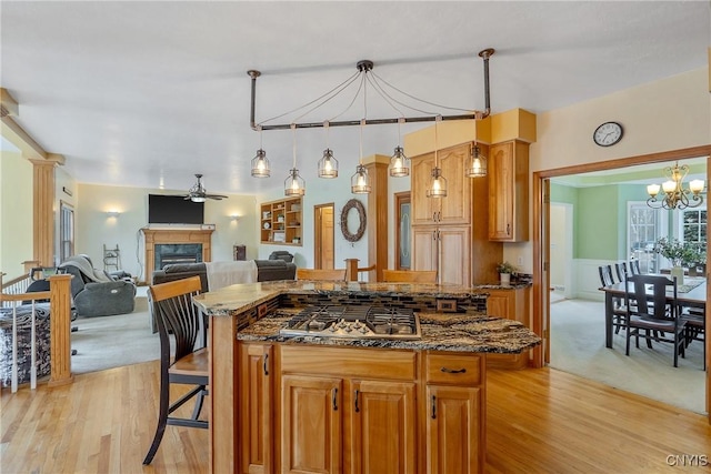 kitchen with a kitchen island, a glass covered fireplace, dark stone counters, stainless steel gas stovetop, and a breakfast bar area