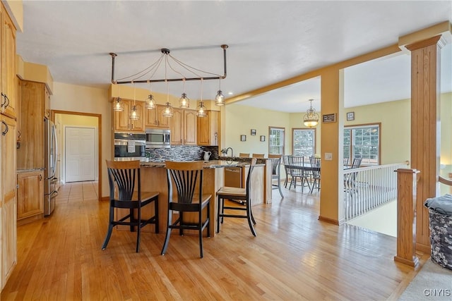 kitchen with a peninsula, light wood-style floors, appliances with stainless steel finishes, a kitchen breakfast bar, and tasteful backsplash