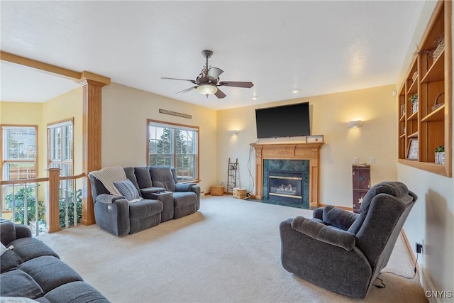 living room featuring baseboards, a premium fireplace, ornate columns, carpet flooring, and a ceiling fan