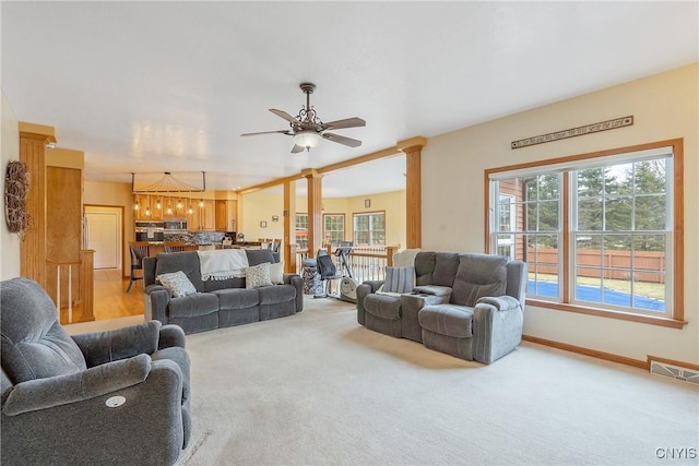 living room featuring baseboards, visible vents, decorative columns, ceiling fan, and light colored carpet