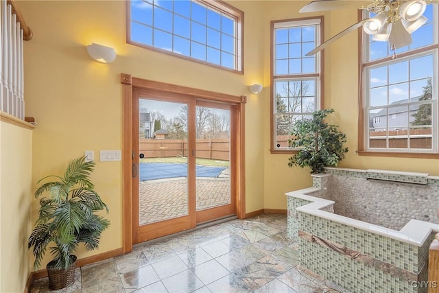 doorway to outside featuring baseboards, a towering ceiling, and a ceiling fan