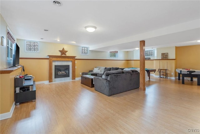 living area with light wood finished floors, visible vents, a tile fireplace, and baseboards