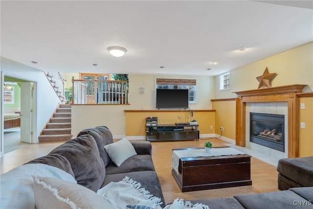 living room featuring stairs, a tiled fireplace, wood finished floors, and baseboards