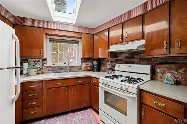 kitchen featuring tasteful backsplash, under cabinet range hood, a skylight, white appliances, and a sink