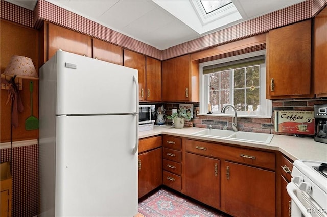 kitchen featuring a sink, white appliances, a skylight, brown cabinetry, and light countertops