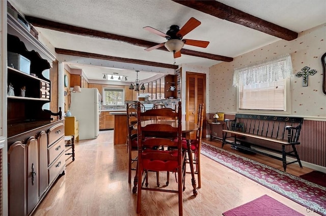 dining room featuring wallpapered walls, a wainscoted wall, beam ceiling, light wood-style flooring, and a textured ceiling