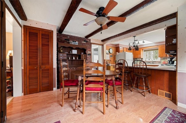 dining room with light wood finished floors, visible vents, beamed ceiling, and ceiling fan with notable chandelier