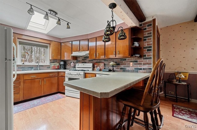 kitchen with white appliances, wallpapered walls, light wood-style flooring, a sink, and under cabinet range hood