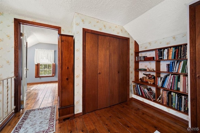 interior space with a textured ceiling, wallpapered walls, lofted ceiling, and hardwood / wood-style floors