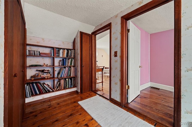 hallway featuring wallpapered walls, wood-type flooring, and a textured ceiling