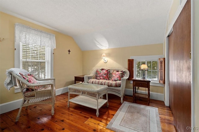 living area featuring a textured ceiling, baseboards, hardwood / wood-style flooring, and vaulted ceiling