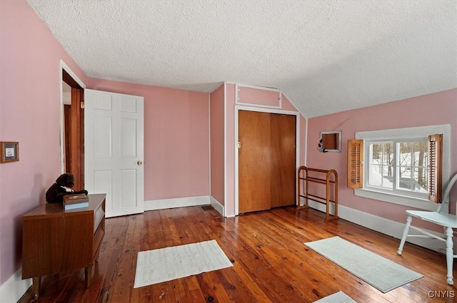 interior space featuring vaulted ceiling, a textured ceiling, baseboards, and hardwood / wood-style floors