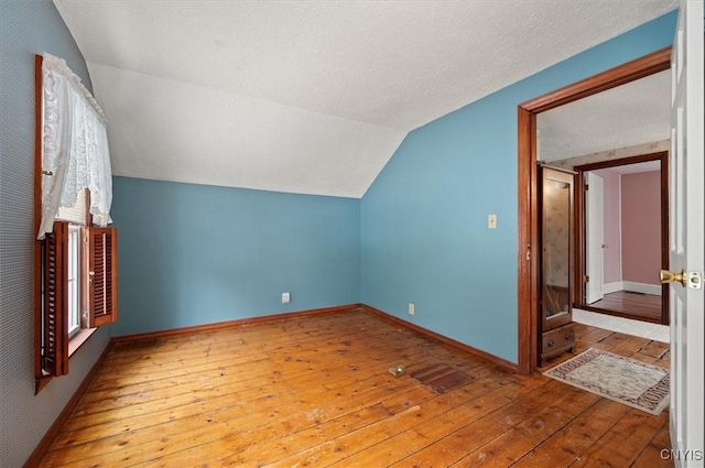 additional living space featuring baseboards, wood-type flooring, a textured ceiling, and vaulted ceiling