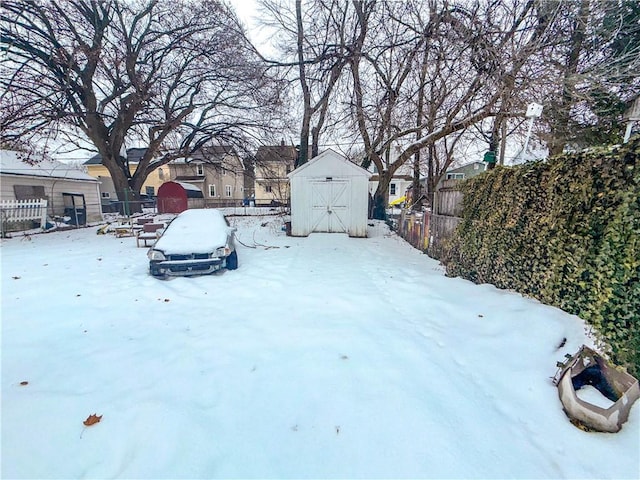 snowy yard featuring an outbuilding, fence, a residential view, and a shed