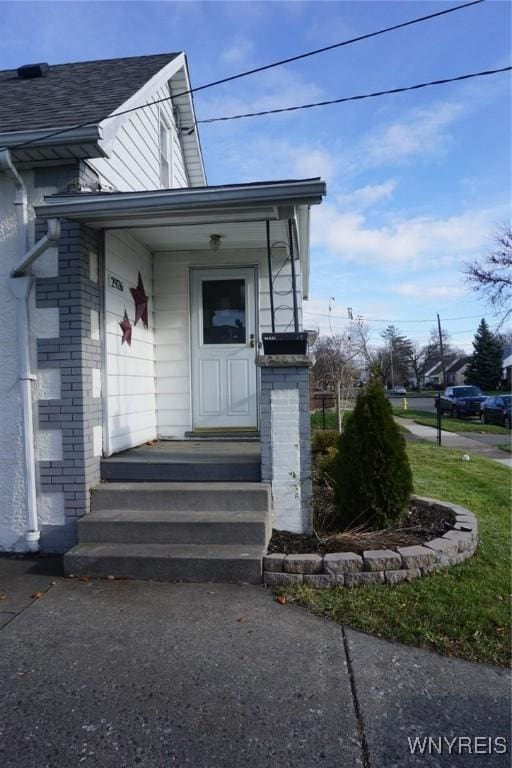 doorway to property with brick siding and a shingled roof