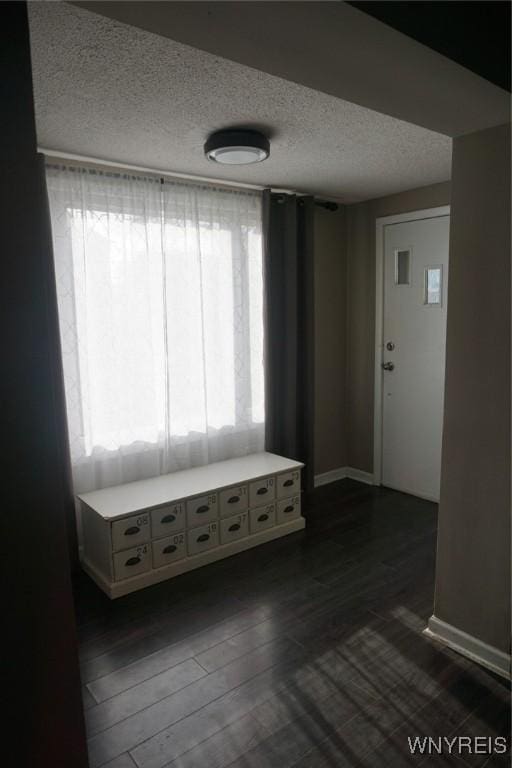 interior space with a textured ceiling, baseboards, and dark wood-style flooring