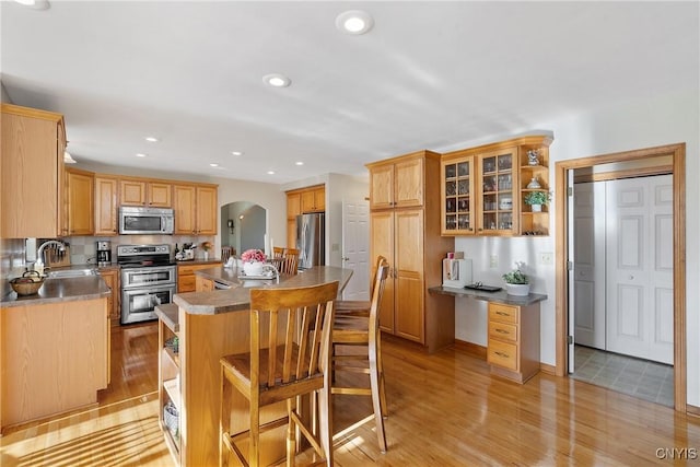 kitchen featuring open shelves, a sink, stainless steel appliances, arched walkways, and light wood finished floors