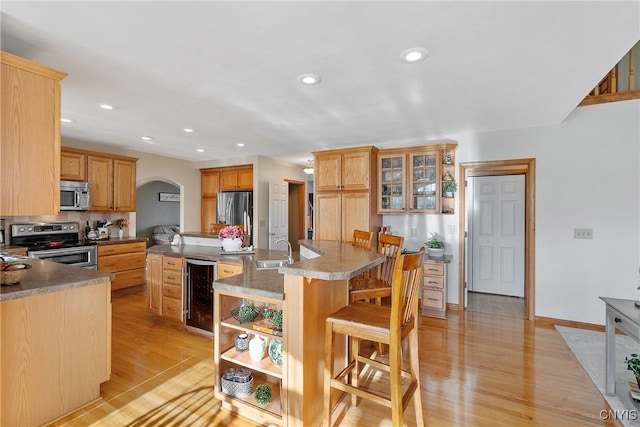 kitchen with beverage cooler, a breakfast bar, an island with sink, a sink, and appliances with stainless steel finishes