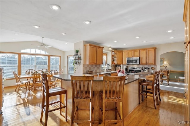 kitchen featuring vaulted ceiling, light wood-style flooring, appliances with stainless steel finishes, arched walkways, and open shelves