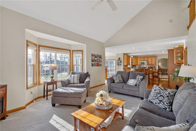 living area featuring baseboards, high vaulted ceiling, arched walkways, ceiling fan, and light carpet