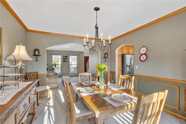 dining area with a wainscoted wall, arched walkways, a chandelier, and crown molding