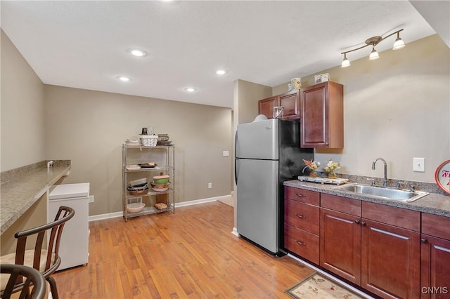 kitchen featuring baseboards, light wood-style flooring, recessed lighting, freestanding refrigerator, and a sink