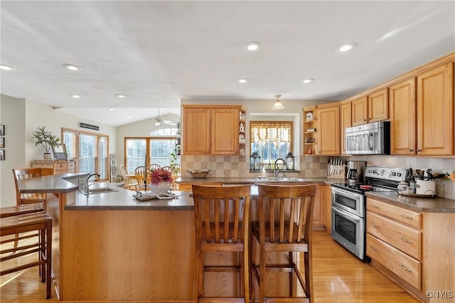 kitchen with a wealth of natural light, a breakfast bar, open shelves, a sink, and appliances with stainless steel finishes