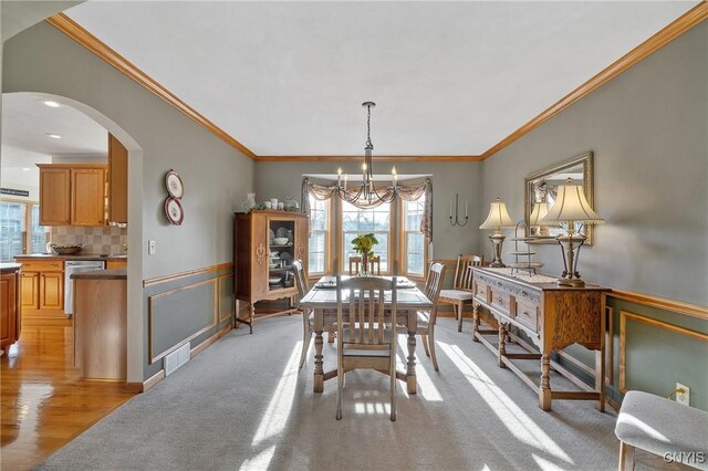 dining room with a wainscoted wall, arched walkways, crown molding, a decorative wall, and a chandelier