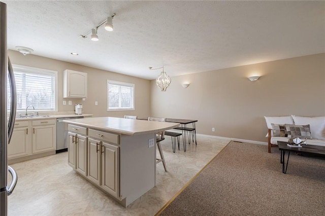 kitchen with a breakfast bar, a sink, a textured ceiling, stainless steel dishwasher, and a center island