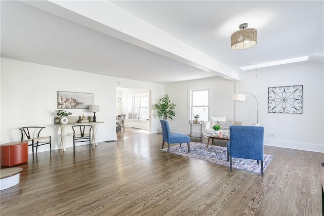 living area featuring beamed ceiling, baseboards, and wood finished floors