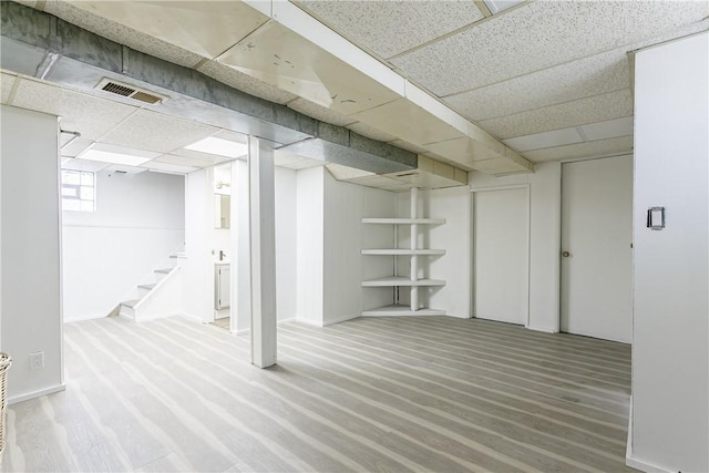 below grade area featuring visible vents, a drop ceiling, stairway, and wood finished floors